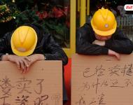 2012年12月25日，廣東中山，火炬開發(fā)區(qū)的多名建筑工人討要工作一年多的血汗錢一籌莫展，一些工人干脆將鋪蓋卷搬到了售樓部，并在門口搭起灶臺煮飯，希望以這種方式討回工錢。圖為在銷售中心門外，工人舉牌討薪。吳進/視覺中國